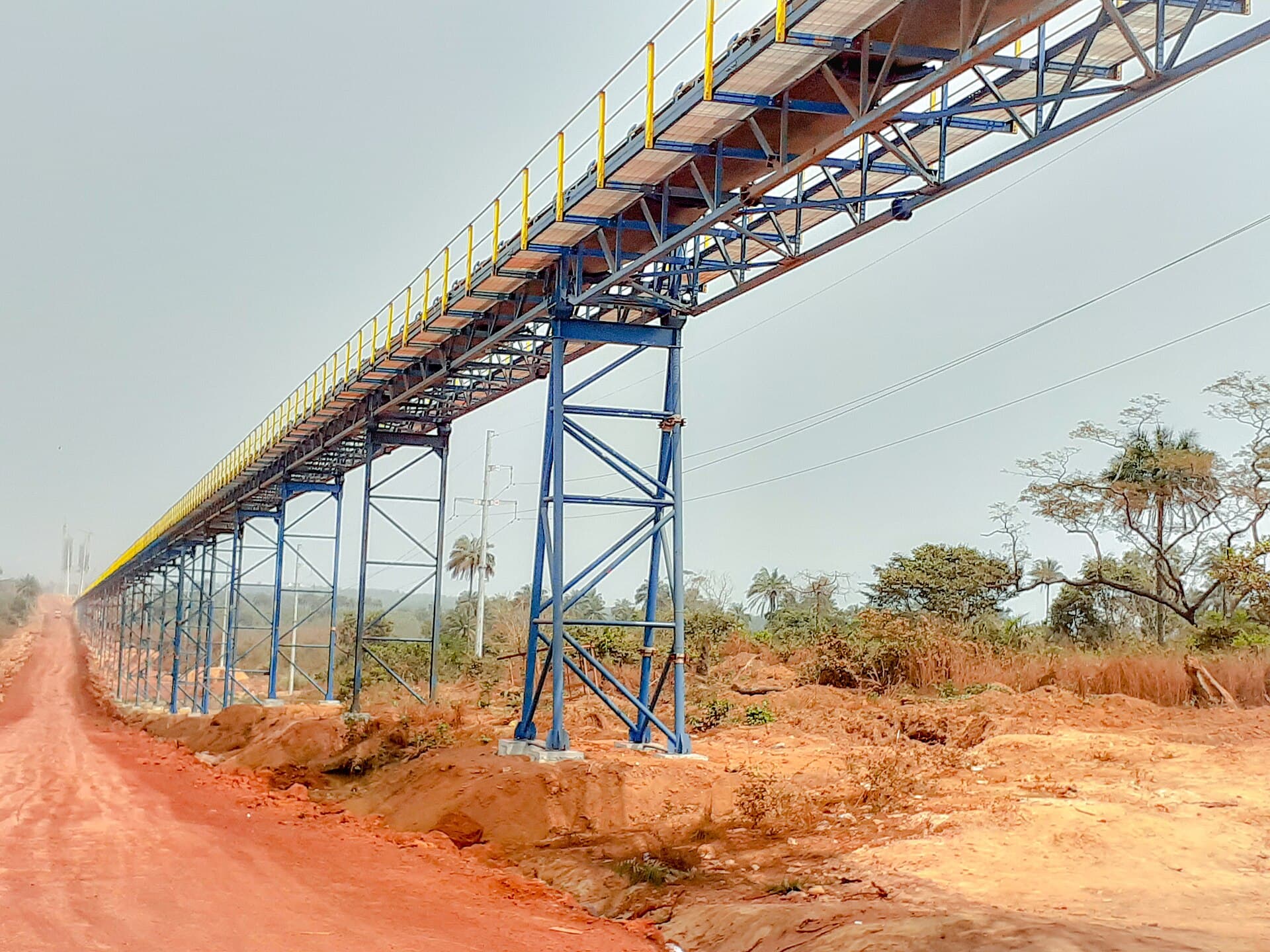 Convoyeur à bande acheminant la bauxite au-dessus d’une piste latéritique, Boffa, Guinée